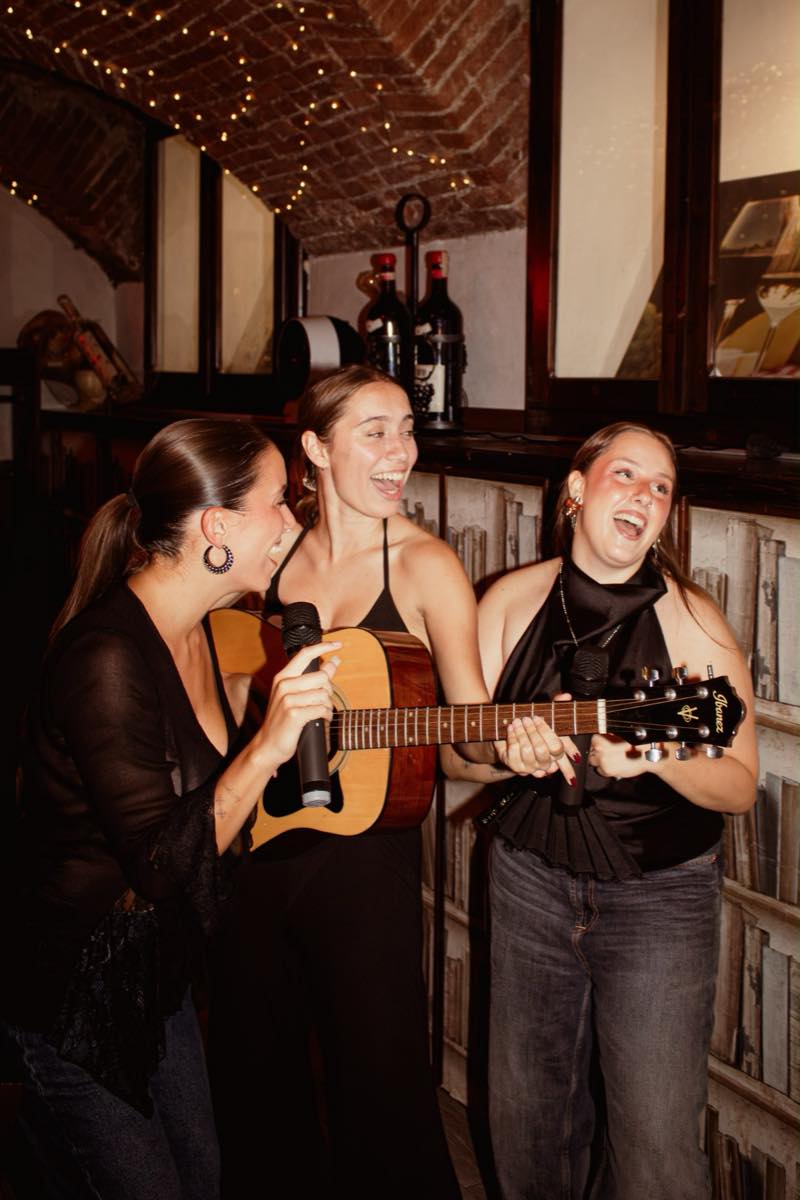 Amiche cantano insieme al microfono con una chitarra durante un addio al nubilato