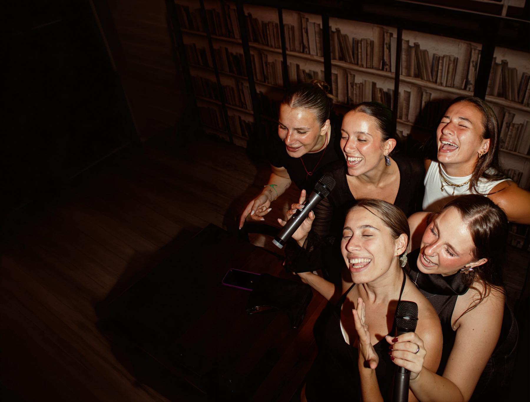Gruppo di amiche canta e ride al karaoke davanti a una libreria